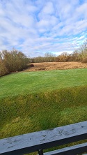 Panoramic view from the balcony showing a vast green field and distant trees under a cloudy sky.