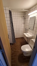 View of the bathroom with white tiled walls, a toilet, a sink, and a shower area with a black and white patterned curtain.