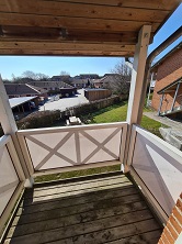View from a small balcony with wooden railings and floor, overlooking a residential area with houses and green spaces.