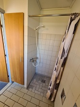 Bathroom with tiled floor and walls, a shower area with a shower curtain, and a wooden cabinet.