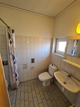 Bathroom with white tiled walls and floor, a toilet, a sink with a mirror, and a shower area with a curtain.