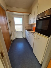 Compact kitchen with blue linoleum floor, white cabinets, a sink, an oven, a refrigerator, and a door leading outside.
