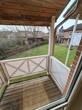 View from a wooden balcony overlooking a green garden and neighboring houses.