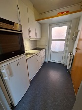 Compact kitchen with white cabinets, a sink, an oven, a refrigerator, and a door leading to the outside.