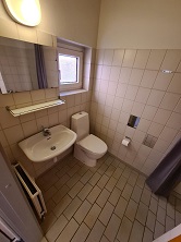 Bathroom with tiled floor and walls, a toilet, a sink with a mirror, and a window.