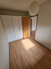 Empty bedroom with light wooden flooring, white built-in wardrobes, and a door leading to another room.