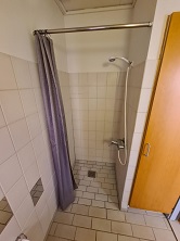 Shower area in a tiled bathroom with a shower curtain and a shower head.