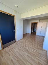 View from the entrance door into an apartment, showing wooden flooring, white walls, and a glimpse of a bathroom and wardrobe in the background.