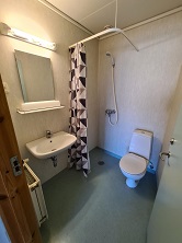 A small bathroom with a toilet, sink, mirror, and shower curtain, featuring light blue flooring and white textured walls.