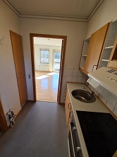 A view from the kitchen looking into the living room, showing the kitchen counter with a sink and hob, and the bright living room beyond.