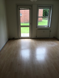 A room with light wooden flooring, a glass door leading to a grassy outdoor area, and a window with a radiator below it.