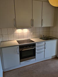 Kitchen counter with an induction hob, oven, sink, and white cabinets.