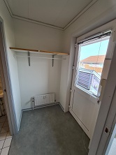 A small entrance or utility area with a window, a shelf, and a clothes rail, leading to an outdoor space.