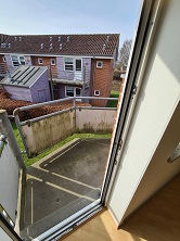 View from an apartment balcony or terrace, showing an outdoor area with a low fence and residential buildings in the background.