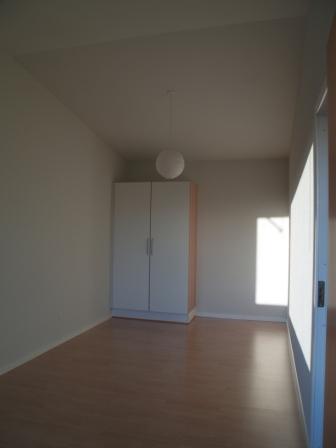Empty bedroom with wooden floor, white walls, a built-in wardrobe, and a window.