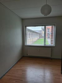 Empty room with light wooden floor, white walls, a large window, and a radiator below it.