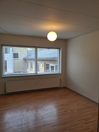 Empty room with light wooden floor, white walls, a large window overlooking a building, and a radiator.