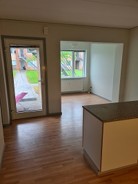 View from a kitchen/dining area towards a living room with a glass door leading outside.