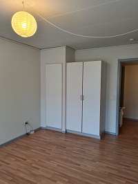 Empty room with light wooden floor, white walls, built-in wardrobes, and a yellow paper lantern.