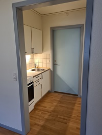 Another view of the kitchen showing a sink, stove, and white tiled backsplash, with a light blue door.