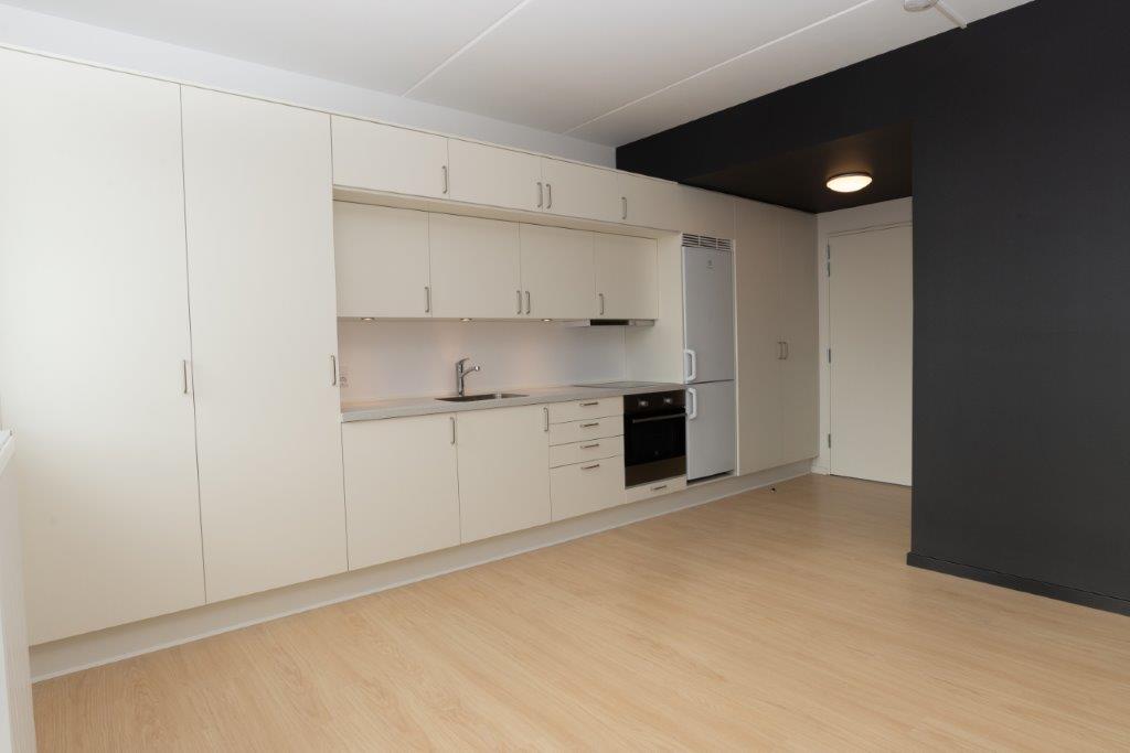 A modern kitchen area with light-colored cabinets, integrated appliances, and a light wooden floor.