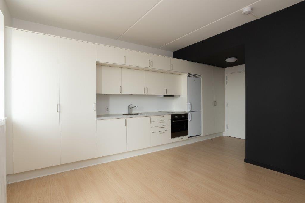 A modern kitchen with white cabinets, integrated appliances, and light wooden flooring in an open-plan living space.