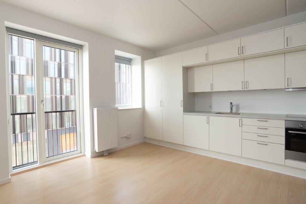 A bright living area with large windows, a radiator, and a view of the exterior, featuring a continuation of the white kitchen cabinetry.