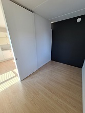 Empty bedroom with light wood flooring, a white sliding door closet, and a dark accent wall.