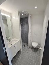 Modern bathroom with white tiled walls, a vanity with sink, mirror, toilet, and a walk-in shower with a grey tiled floor.