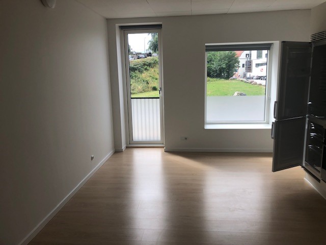 Living room area with light wood flooring, a large balcony door, and a window overlooking a green outdoor space.