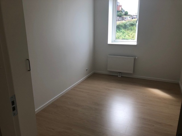 Empty bedroom with light wood flooring, a window, and a radiator, showing a simple and clean design.