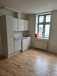 A compact kitchen area with white cabinets, a sink, a small refrigerator, and a window with a radiator below.