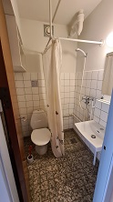A compact bathroom with a toilet, a small sink, a shower area with a curtain, and tiled walls and floor.