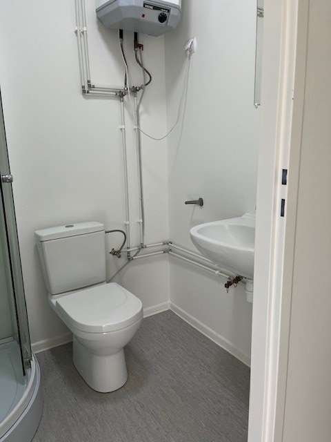 Bathroom with a white toilet, wall-mounted sink, and exposed plumbing leading to a water heater.