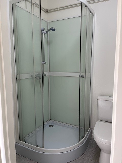 Corner shower cabin with glass doors and a shower head, located next to a toilet in a small bathroom.
