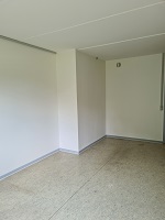 An empty, unfurnished room with light-colored walls and a light-colored floor, showing a corner view.