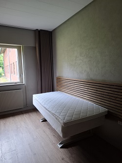 A bedroom with a single bed set against a wooden slat headboard, next to a window with a radiator below.