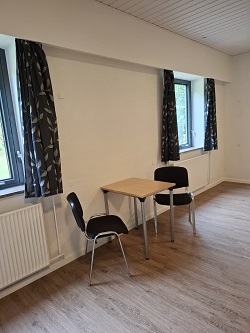 A bright room with a small table, two chairs, and windows with dark curtains.