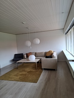 A living room with a beige sectional sofa, a coffee table, a dark armchair, and three white spherical pendant lights.