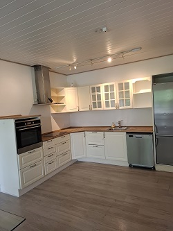 A modern kitchen with white cabinets, a stainless steel range hood, built-in oven, and a large refrigerator.
