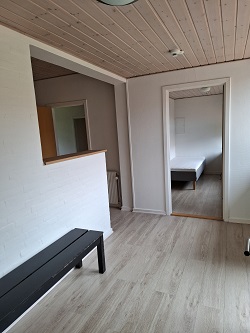 An interior hallway or entrance area with a black bench, leading to another room with a bed visible through a doorway.