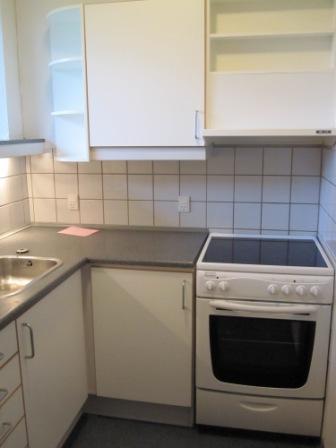 A close-up view of a kitchen counter with a sink, white cabinets, and a white electric stove.