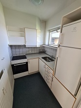 A compact kitchen with white cabinets, a sink, an electric stove, and a tall white refrigerator.