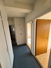 A narrow entrance hallway with blue carpet, white built-in wardrobes, and doors leading to other rooms.