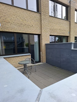 Outdoor patio with a small table and chair, surrounded by brick walls and large windows.