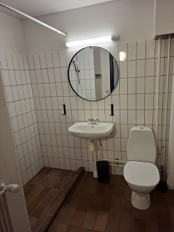 Modern bathroom with white tiled walls, a round mirror, sink, and toilet.