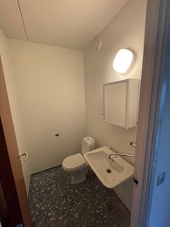 A small toilet room with a white toilet, a wall-mounted sink, and a mirrored cabinet, featuring dark patterned floor tiles.