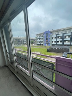 View from a balcony with sliding glass doors overlooking an apartment complex and green space under a cloudy sky.