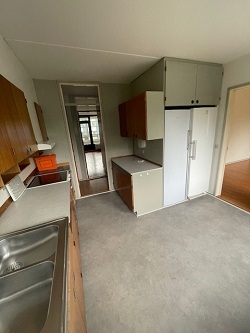 A kitchen with light grey floor, wooden cabinets, a double stainless steel sink, and a white refrigerator.