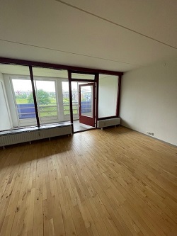 A bright living space with hardwood floors, large windows, and a glass door leading to a balcony.